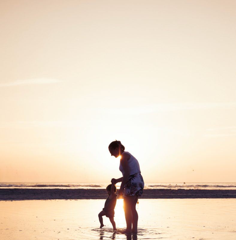 woman walking with child on a beach at sunset