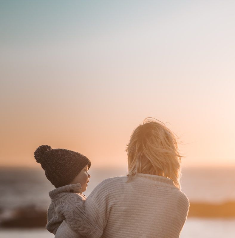 Woman holding child looking out at a sunset on the beach